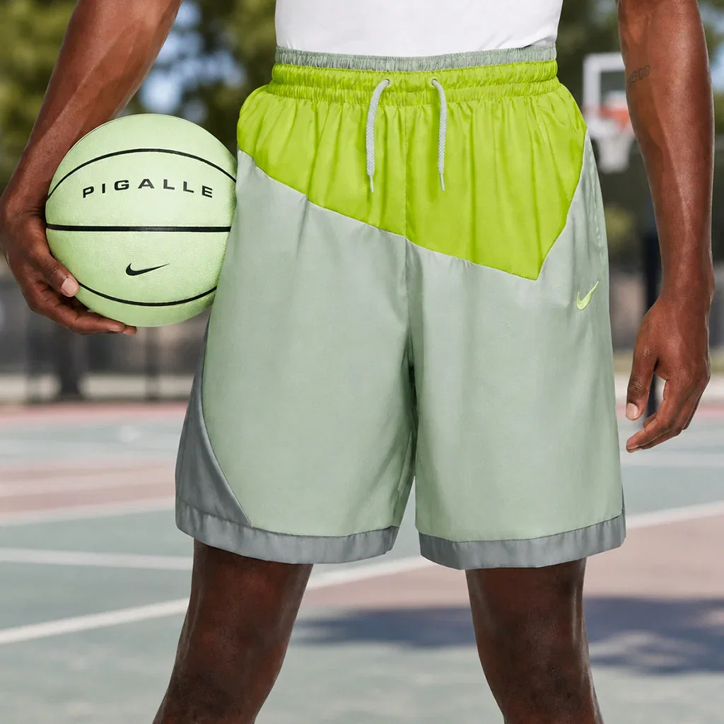 Athlete holding a lime green Nike Pigalle basketball while wearing matching neon yellow and gray basketball shorts on court.