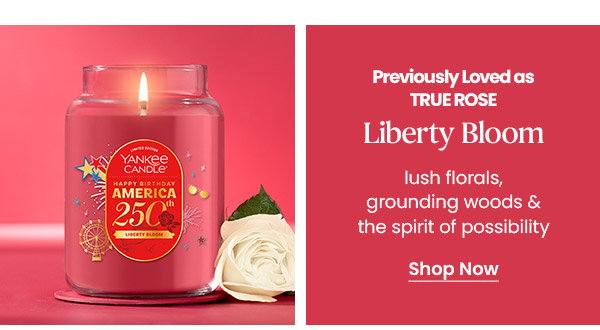 Red Yankee Candle jar labeled America 250, text about Liberty Bloom scent and a Shop Now button, white rose beside candle.