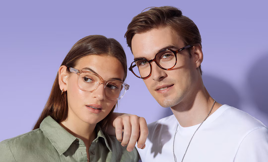 Man in tortoiseshell glasses with his hand on a woman's shoulder; she wears light cat-eye glasses, against a purple background