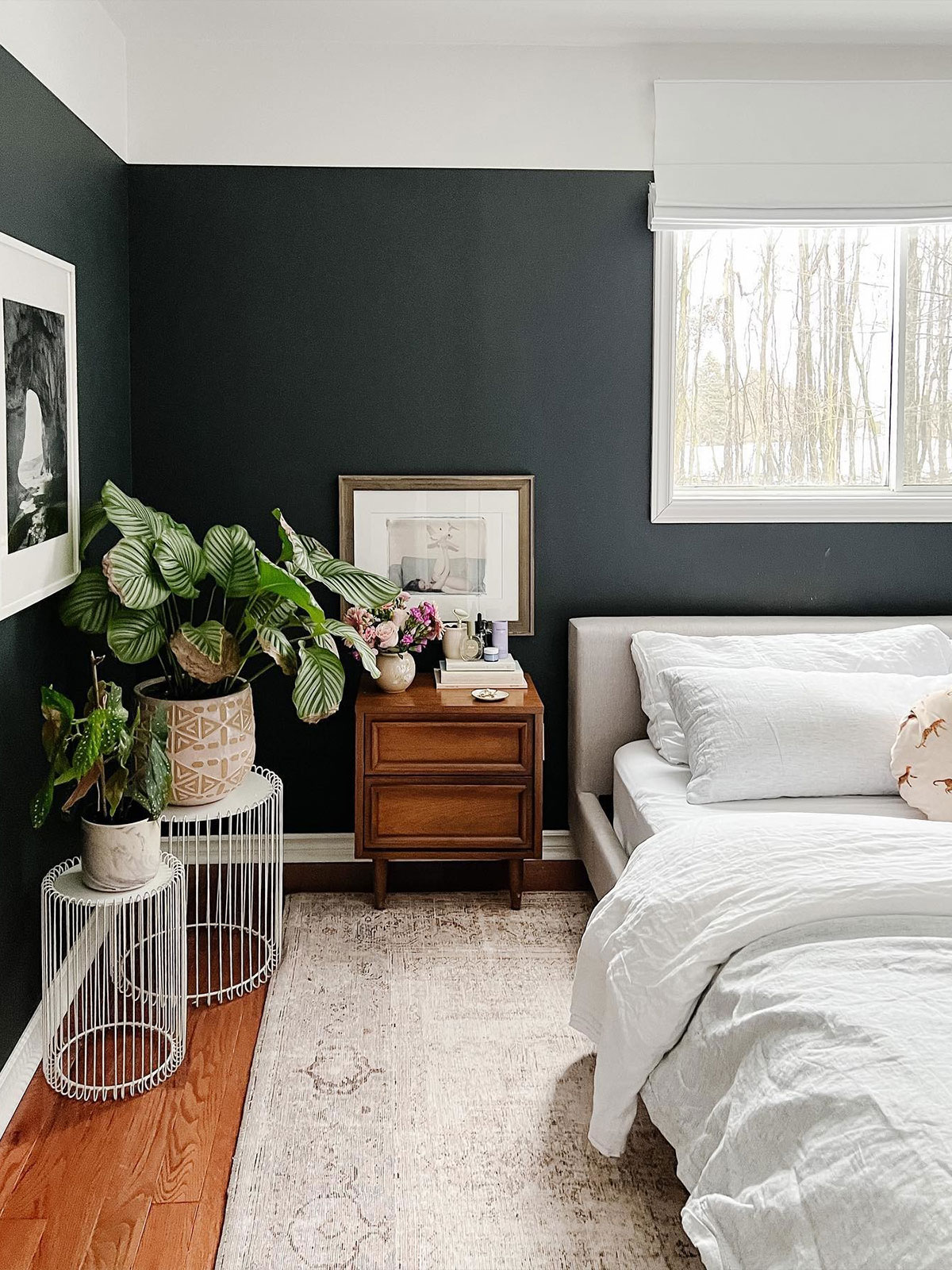Moody black walls wrap this bedroom in a cocoon-like calm. The dark walls are contrasted with crisp white bedding, and complemented by warm wood and leafy plants, for a room that feels fresh, balanced and effortlessly serene.