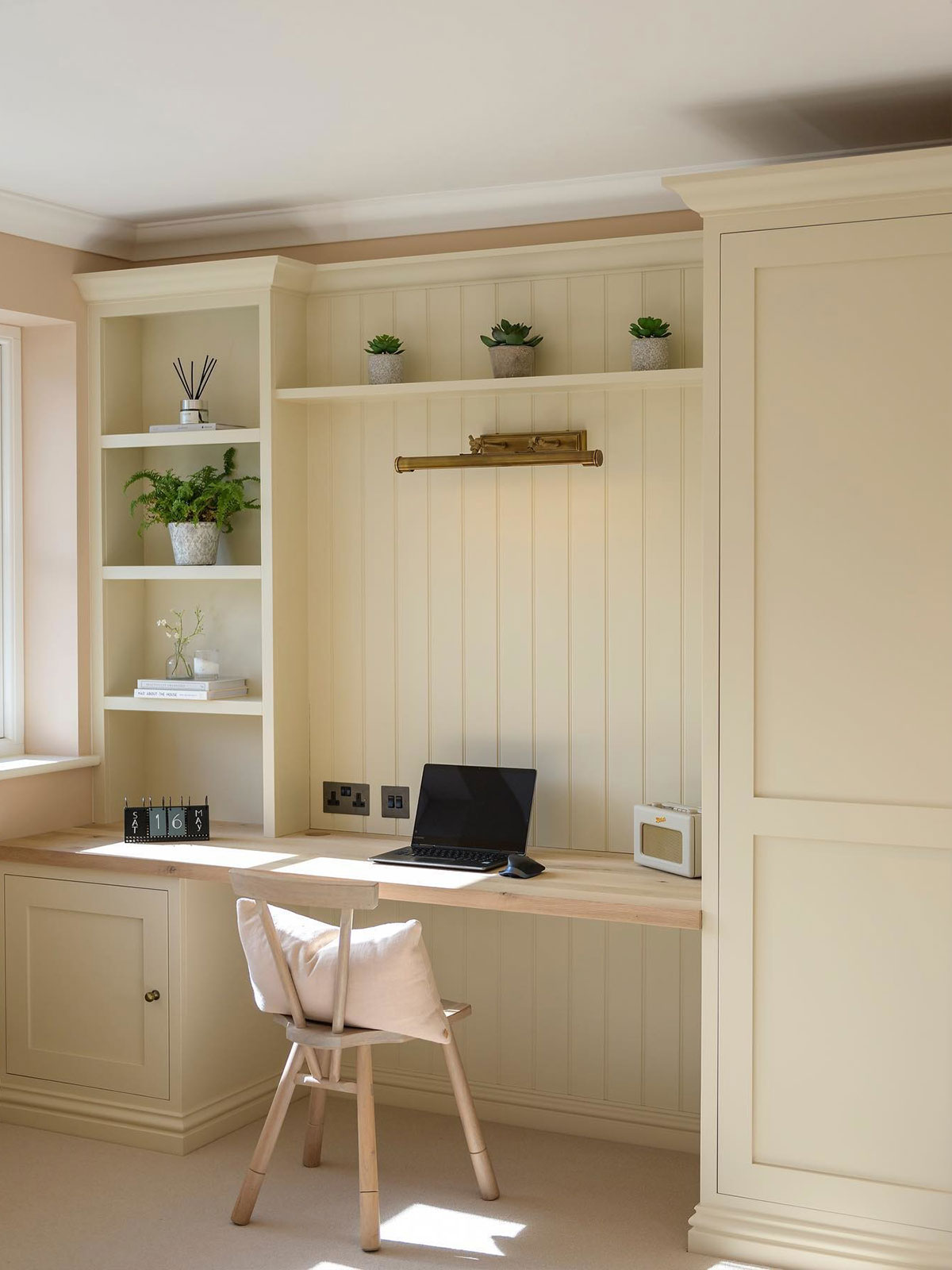 Soft neutrals and sunlit surfaces make this workspace feel quietly uplifting. A simple wooden desk sits in front of wooden panelling and built-in shelves, all in the same creamy tones. It’s a calm, uncluttered space that’s built for focus.