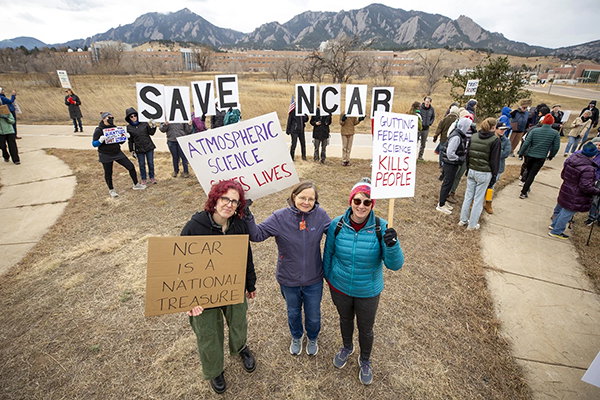 Protesters hold signs in support of NCAR against a background of Boulder’s iconic mountains.