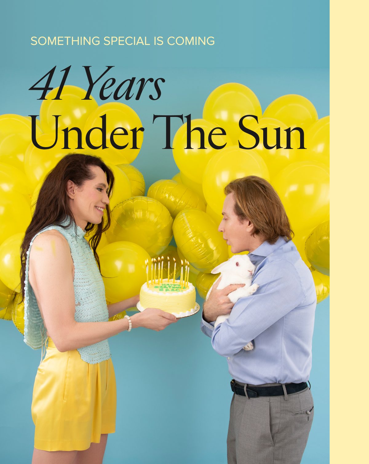 A woman holds a birthday cake with candles while Eric looks on, surrounded by yellow balloons.