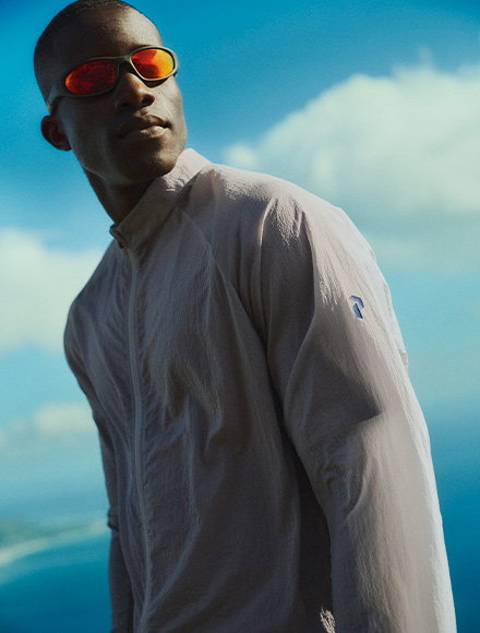 Image of a man wearing a hiking jacket and sunglasses with red lenses, with blue sky in the background.