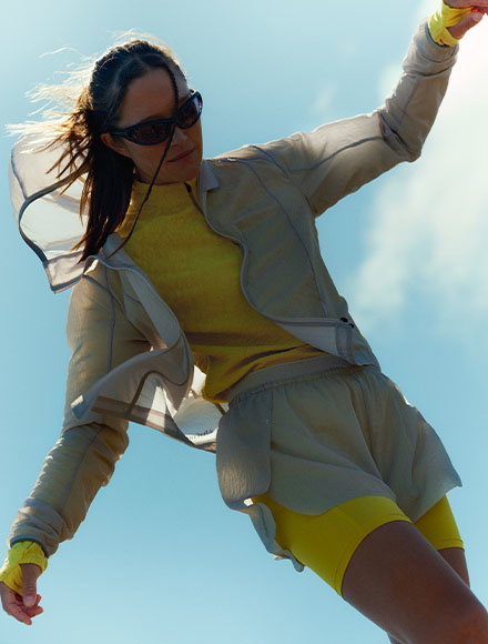 Image of a woman in hiking clothing and sunglasses, with her jacket lifted by the wind and appearing to be balancing.