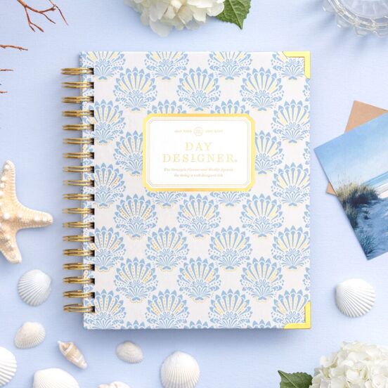 repeated blue and gold shell pattern, day designer planner, light blue background with shells, white flowers and pictures