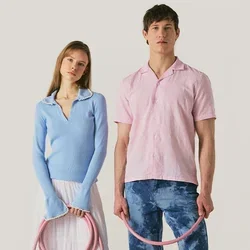 Vrouw in blauwe trui en witte rok en man in roze overhemd en blauwe spijkerbroek houden een opgerolde roze slang vast, staand op een lichte achtergrond.