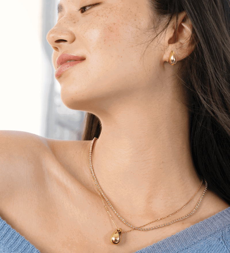 Female model wearing layered yellow gold necklaces and matching teardrop stud earrings.