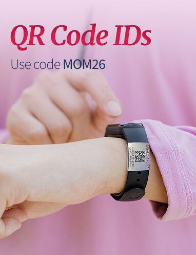 Close-up of a wrist wearing a black sports band with a silver MedicAlert metal tag. The tag features the MedicAlert logo and a QR code. A second hand is visible pointing towards the QR code. Red title text reads 'QR Code IDs'. Below the title, smaller text says, 'Use code MOM26'.