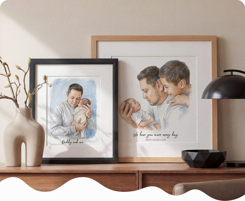 Two framed watercolour illustrations of fathers with their babies displayed on a sideboard, one in a black frame and one in a natural wood frame