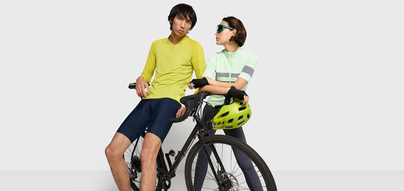 Équipement de cyclisme montré : une personne portant un haut jaune et un short marine, une autre dans un haut rayé vert clair et un pantalon gris, avec un casque vert sur un vélo noir.