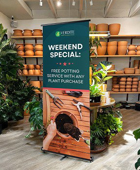 A retractable banner inside a plant shop advertises free potting services alongside potted plants and planters lining the store shelves.