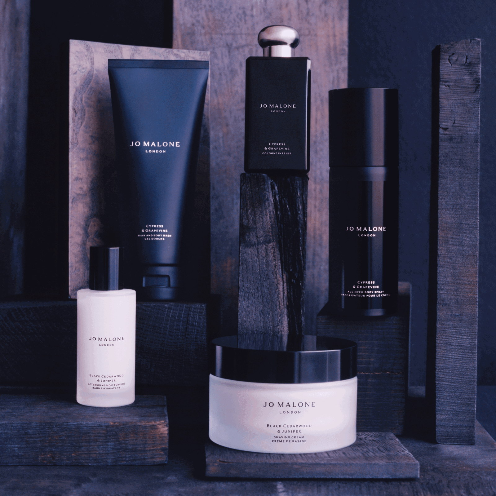 Jo Malone's grooming products displayed on chunks of blue wood, against a dark blue background.
