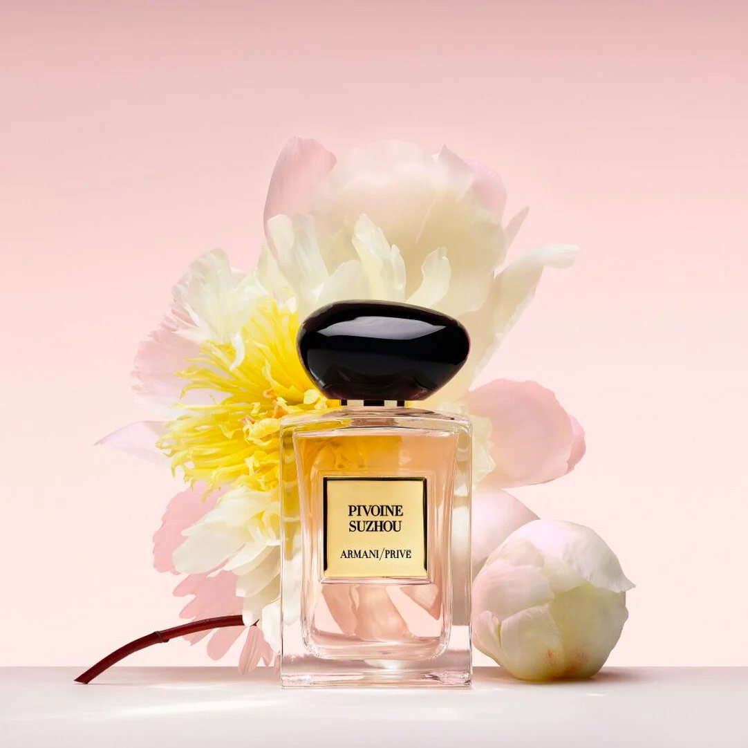 Frasco de perfume Armani Privé Pivoine Suzhou presentado delante de peonías blancas y rosa suave sobre un fondo rosa pálido.
