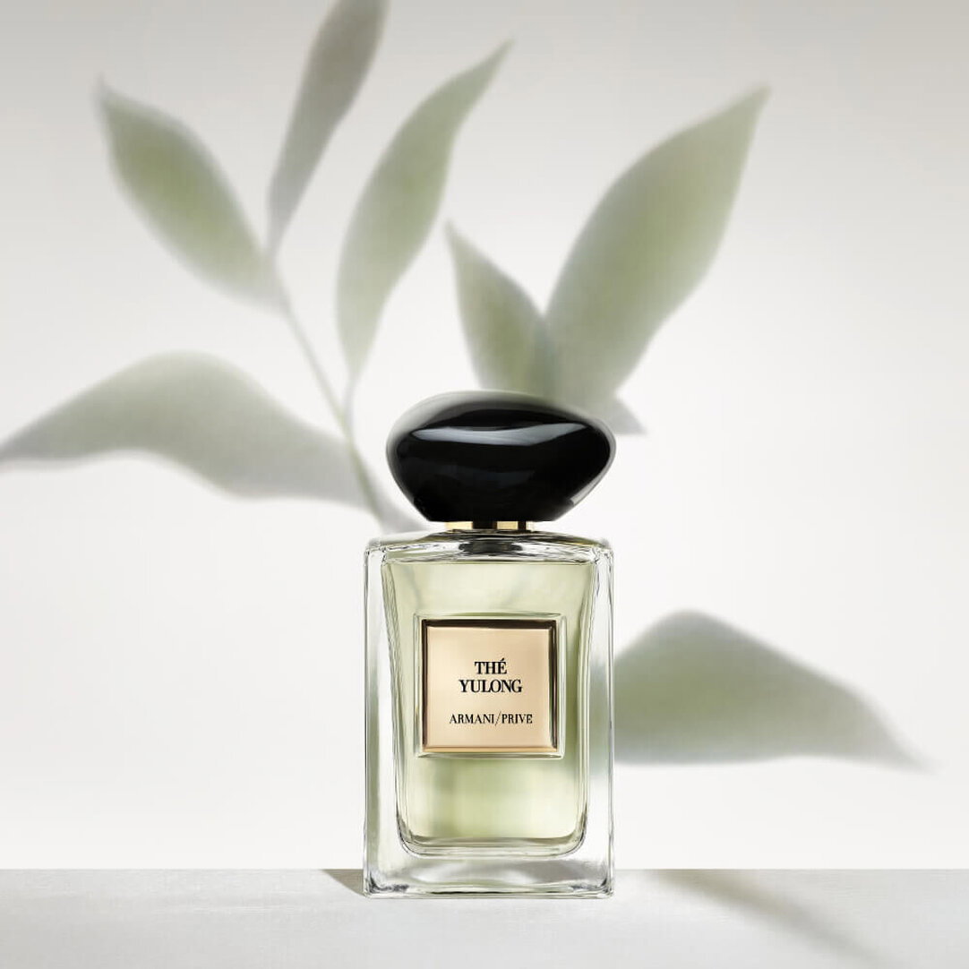 Frasco de perfume Armani Privé Thé Yulong presentado solo sobre un fondo claro, con suaves sombras de hojas verdes al fondo.