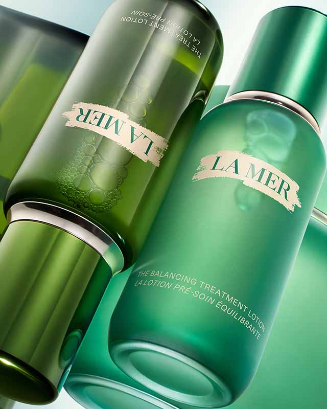 Two green La Mer skincare bottles with silver accents, laying diagonally.