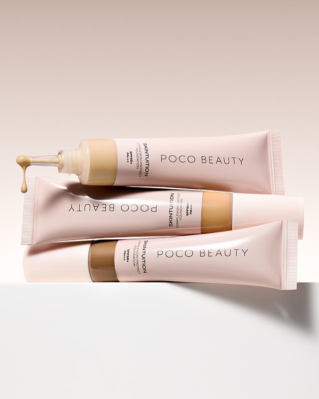 Three tubes of Poco Beauty foundation in soft pink packaging, one with a pump nozzle, displayed on a white surface.