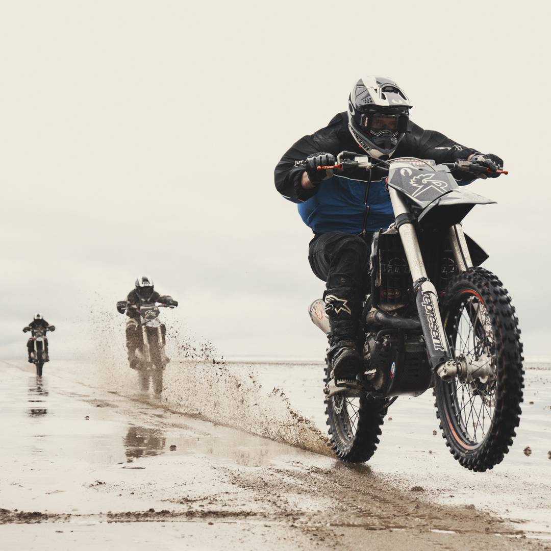 Models riding branded Represent x Belstaff motorcross bikes across the Pendine Sands