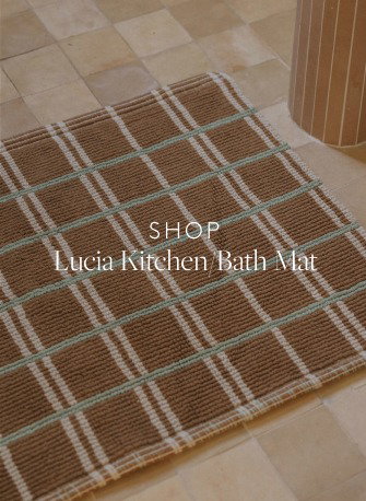 Brown bath mat with teal and cream checks on a tile floor