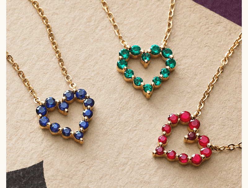 Colorful heart shaped gemstone pendants rest on a playing card.