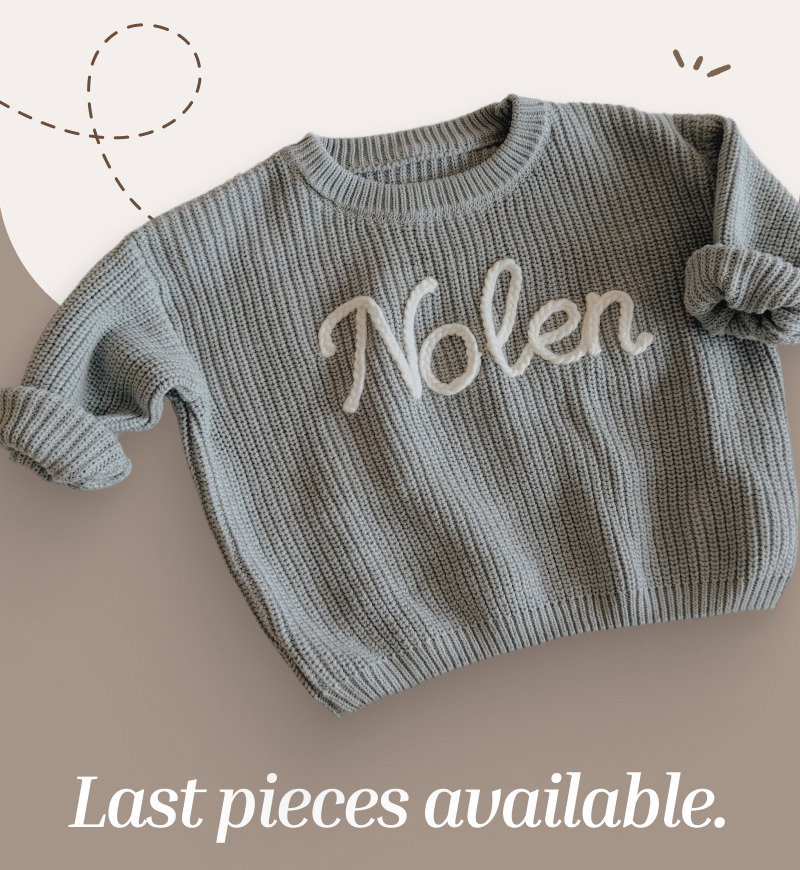 Flat lay of a knitted baby sweater with stitched name on a soft neutral background beside centered serif title text