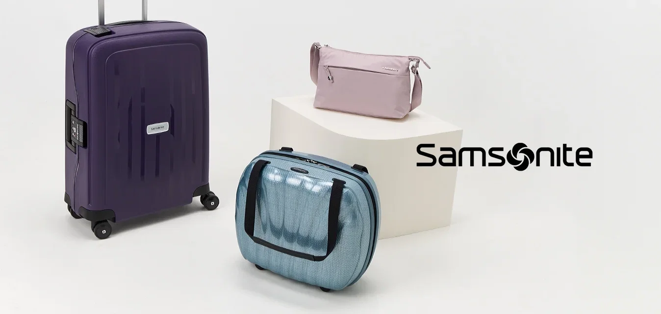 Drie stukken bagage: een paarse rolkoffer, een blauwe handbagage en een roze make-up tas, tentoongesteld op een witte ondergrond.