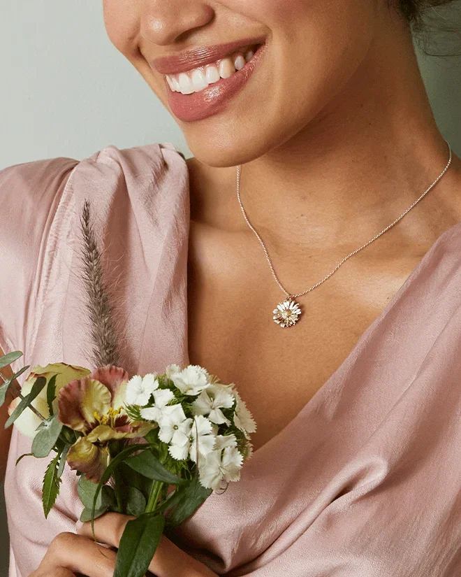 Model in a pink dress holding flowers, wearing a mixed metal daisy necklace