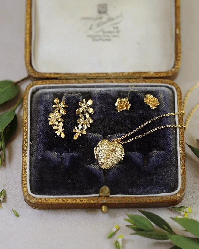 Jewellery box with three gold-plated pieces: a heart locket, posy earrings, and rose stud earrings