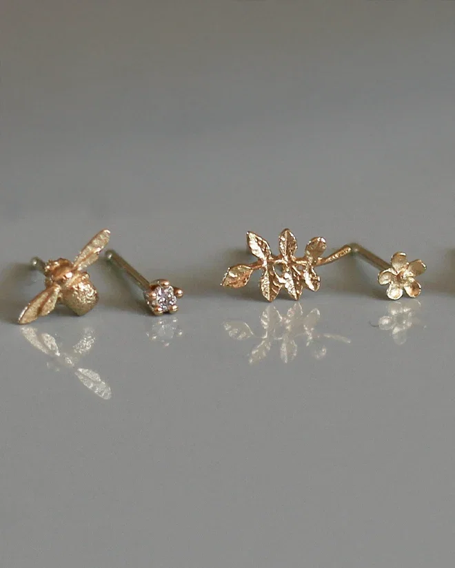 Set of four Teeny Tiny stud earrings featuring a gold bee, sparkling diamond, delicate leaf, and dainty posy flower