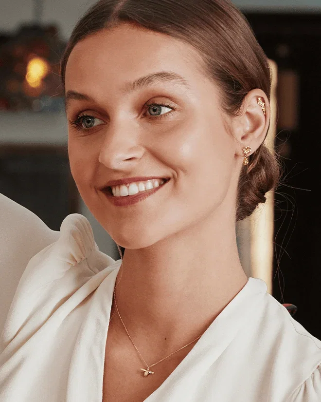 Model in a white dress wearing a delicate gold bee necklace from the Teeny Tiny collection