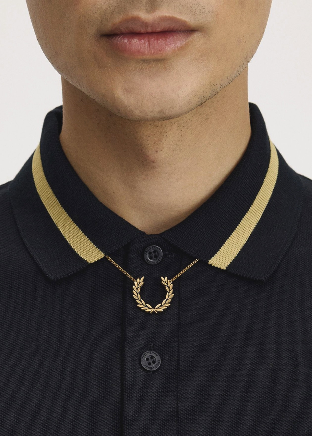 Close up of a model wearing a M2 Made In England Fred Perry Shirt in Black / Champagne and a Laurel Wreath Necklace in Gold