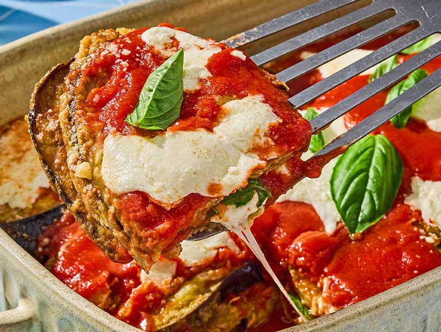 A slice of eggplant parmesan being lifted from the rest of the casserole in a casserole dish.
