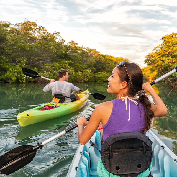 A man and a woman kayak through green mangroves.