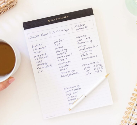 white notepad with black trim tape, shown with written on page, coffee, corner of planner binding