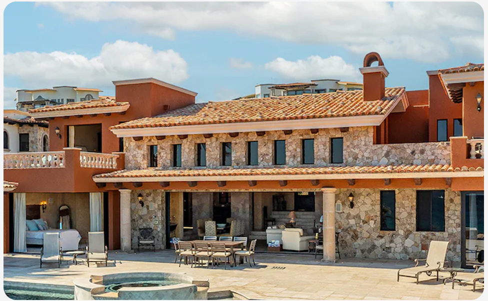 Stone‑front residence with covered outdoor seating, a pool, and patio furniture along the exterior.