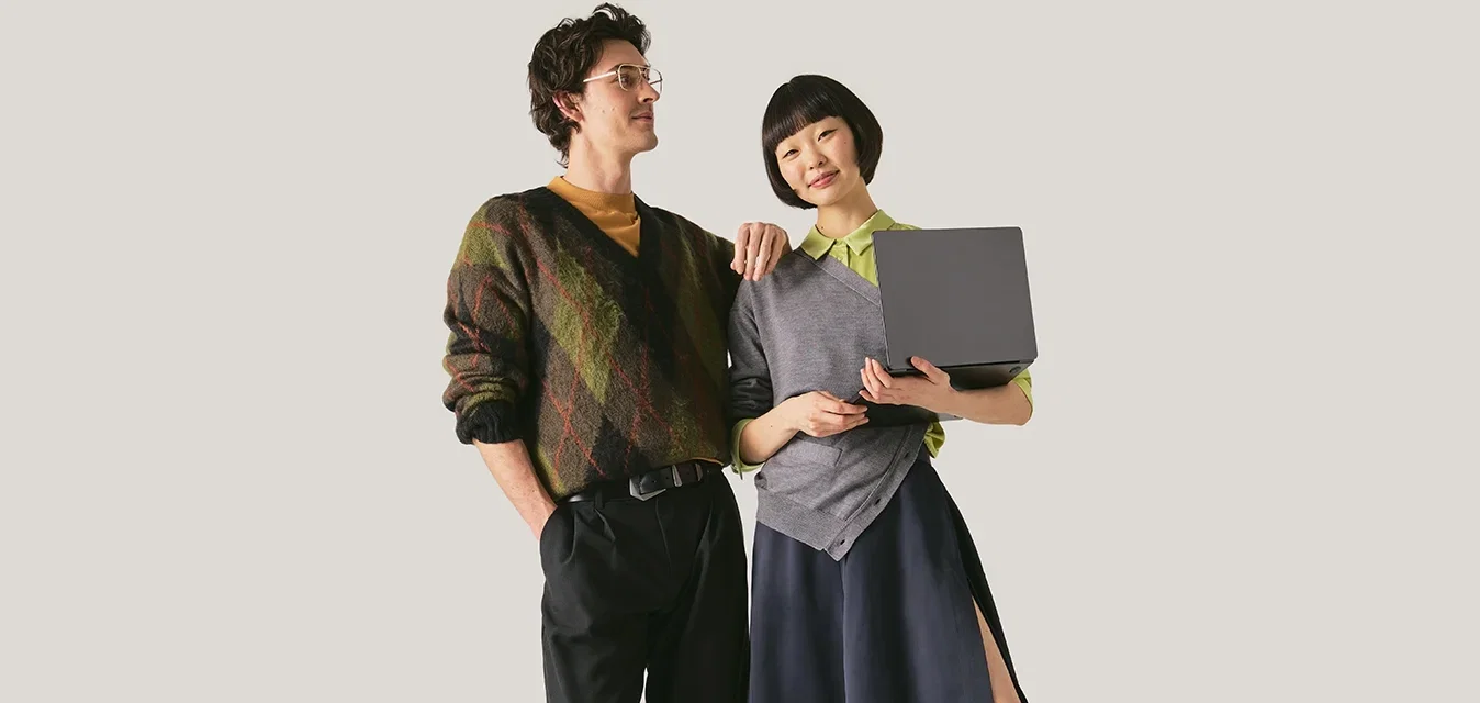 Jeune homme et femme debout côte à côte, la femme tenant un ordinateur portable noir fermé, tous deux vêtus de tenues décontractées et modernes.