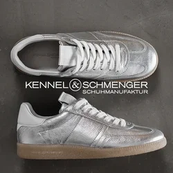 Metallisch silberne Sneaker mit strukturiertem Obermaterial, weißen Schnürsenkeln und einer hellbraunen Gummisohle, die minimalistische Designelemente und Nähdetails aufweisen.