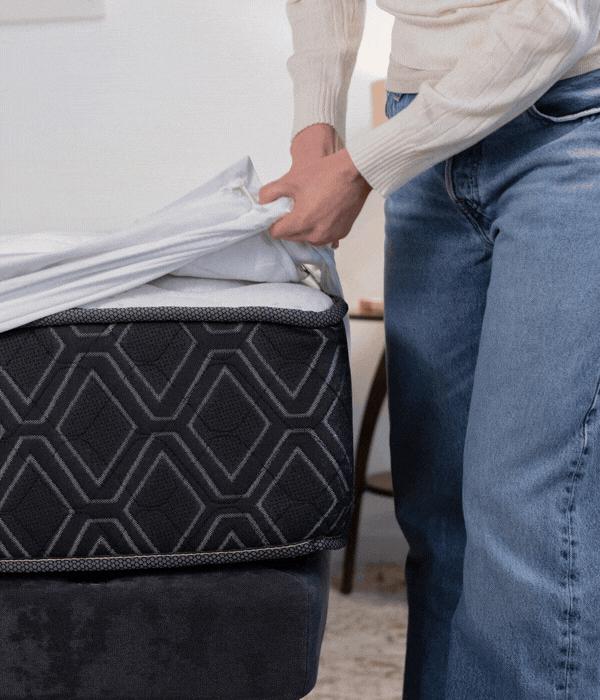 A woman pulls her fitted sheet over the mattress corner