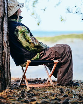 Man sits on the SOLUPPGÅNG stool at a campground.