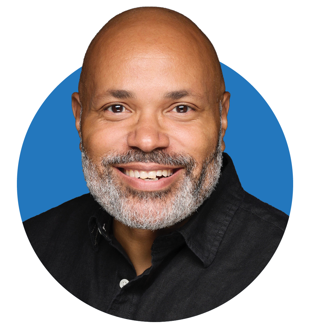 A man with a bald head, white beard, and black shirt smiling at the camera.