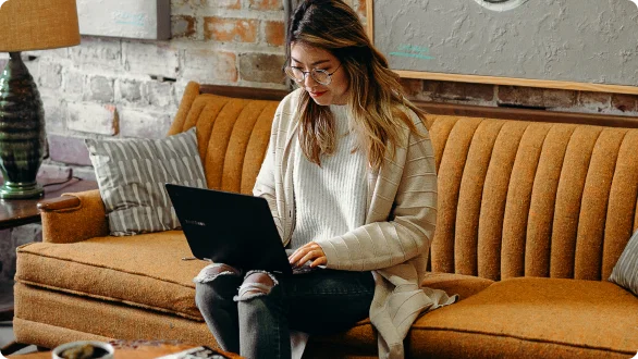 Person sitting in a brown couch while working in a laptop