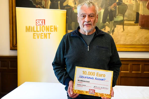 Ein Mann hält einen großen Scheck über 10.000 € in die Kamera. Im Hintergrund ist das Logo des SKL Millionen-Events