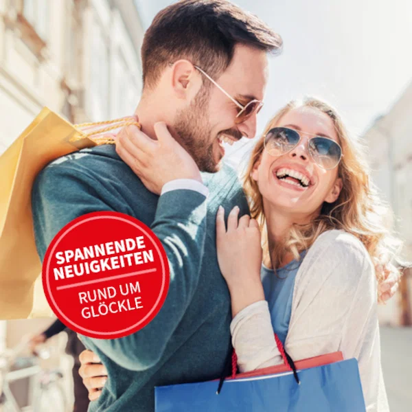 Ein Mann und eine Frau, beide mit Einkaufstaschen, halten sich lachend im Arm.