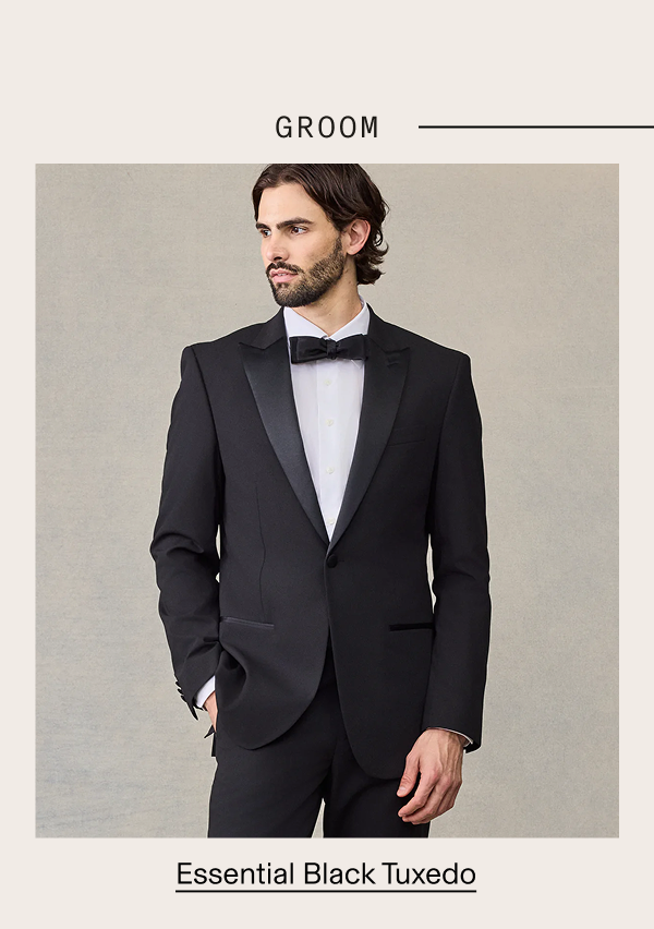 Man wearing a black tuxedo jacket with satin peak lapels, white dress shirt, and black bow tie, against a neutral background. GROOM —. Essential Black Tuxedo
