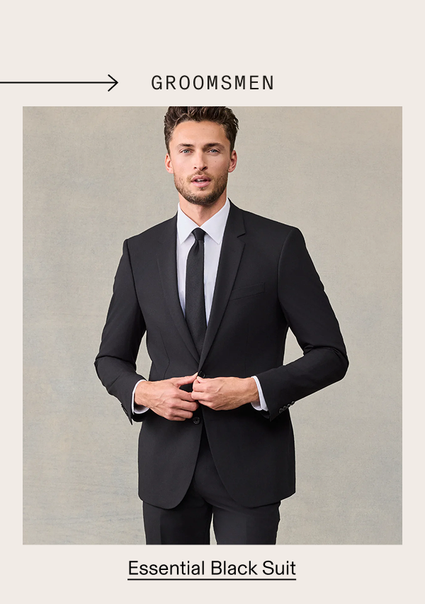 Man wearing an essential black suit jacket, white dress shirt, and black tie, against a neutral background. → GROOMSMEN. Essential Black Suit