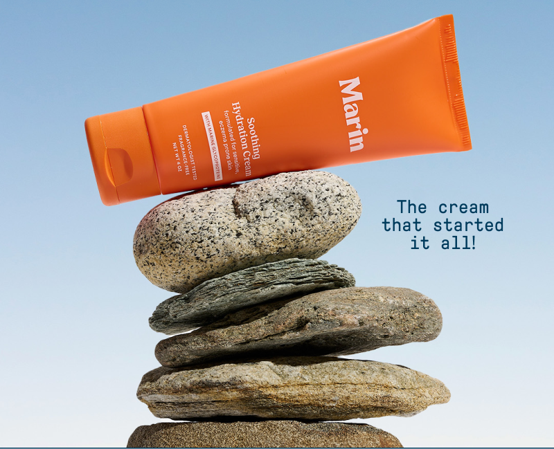 An orange tube of Marin Soothing Hydration Cream balanced atop a stack of smooth coastal rocks against a blue gradient background. Text beside the product reads, “The cream that started it all!”