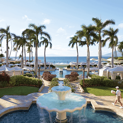 Scenic view of a fountain and palm trees lining a pathway to the ocean.