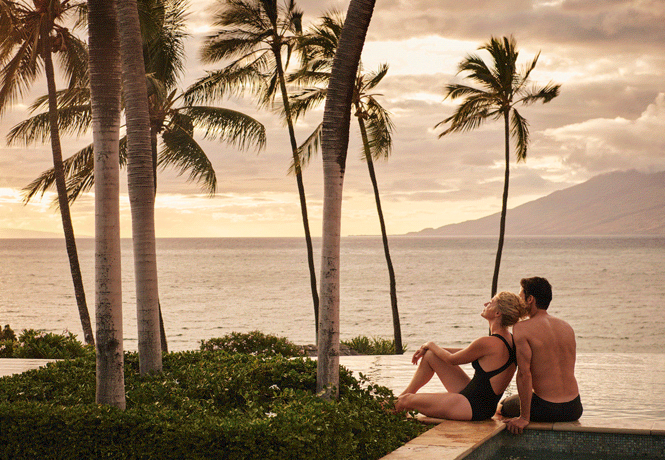 Hero GIF featuring 4 frames: 1) A couple lounging by the infinity pool, watching the sun set over the ocean. 2) Chic living room with floor-to-ceiling windows that overlook the seascape. 3) A group of friends making a toast at dinner in an elegant outdoor setting. 4) Panoramic view of beautifully landscaped gardens, with the ocean and a volcano in the background.
