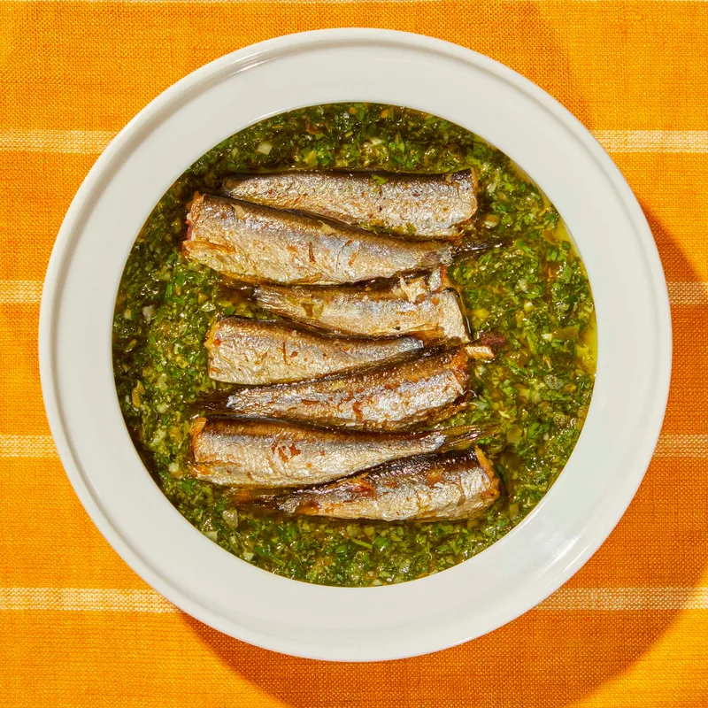 Fried sardines in salsa verde on a white plate.