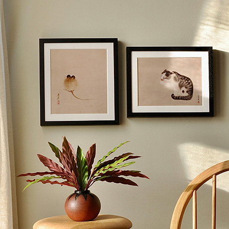 Two Japanese animal-themed prints, one featuring a mouse and the other a cat, framed in black and hung on a light wall – Prints and Postcards Collection.